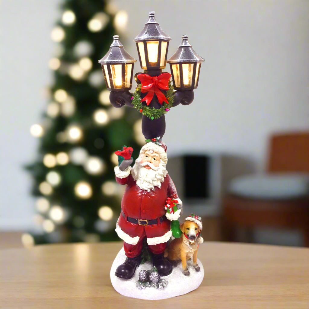 Decorative Christmas figure with Santa Claus, dog, and street lamp on a white background