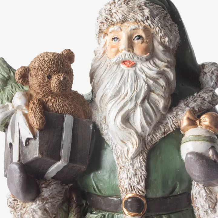 Statue of a bearded figure in a green robe holding a teddy bear and a bag.