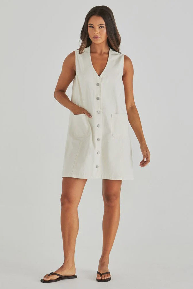 Woman wearing a white sleeveless denim dress on a plain background
