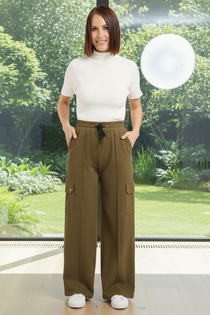 Woman wearing olive green cargo pants and a white top on a light gray background