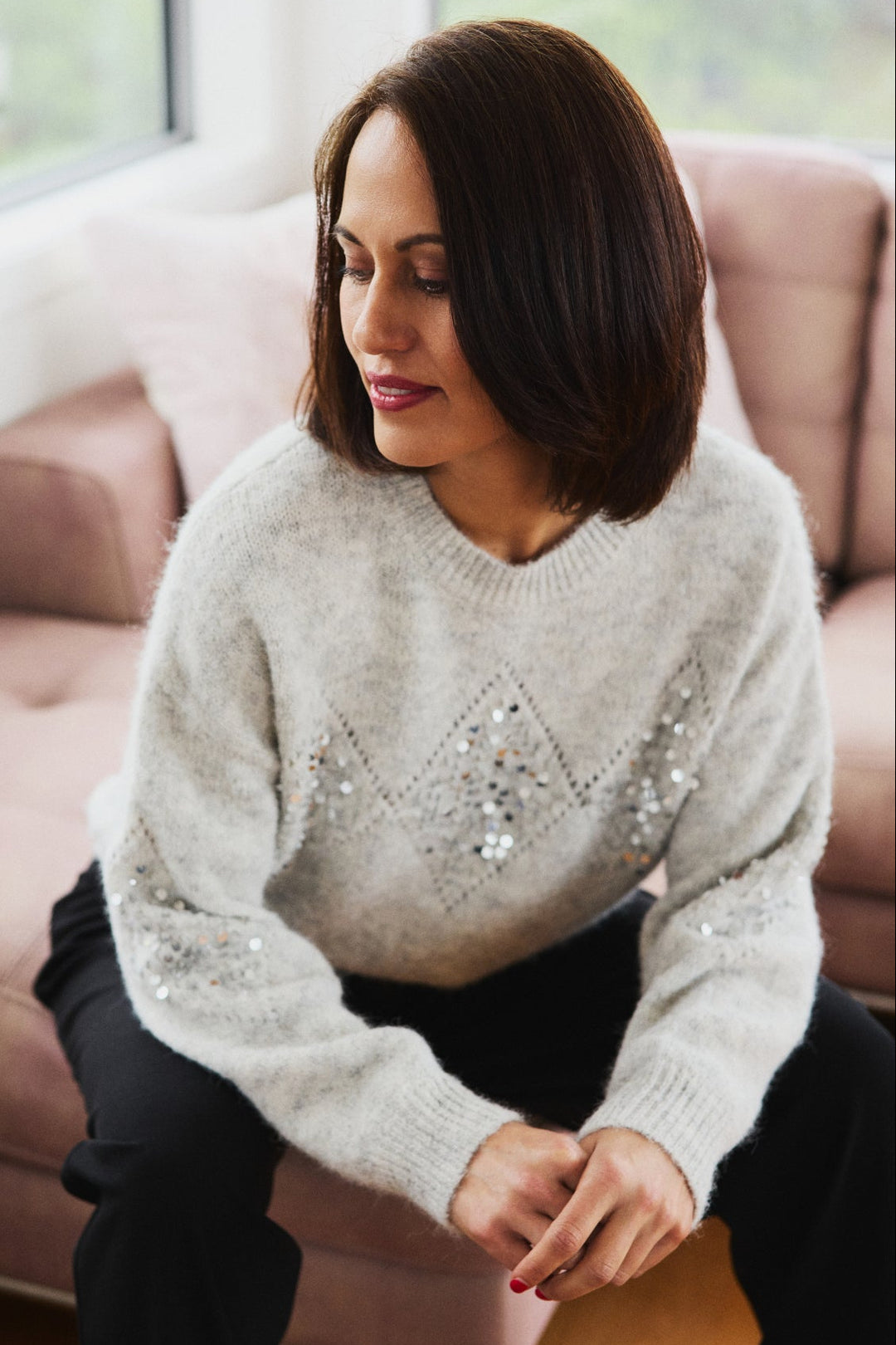 Woman wearing a light gray sweater with sequin details sitting on a couch.