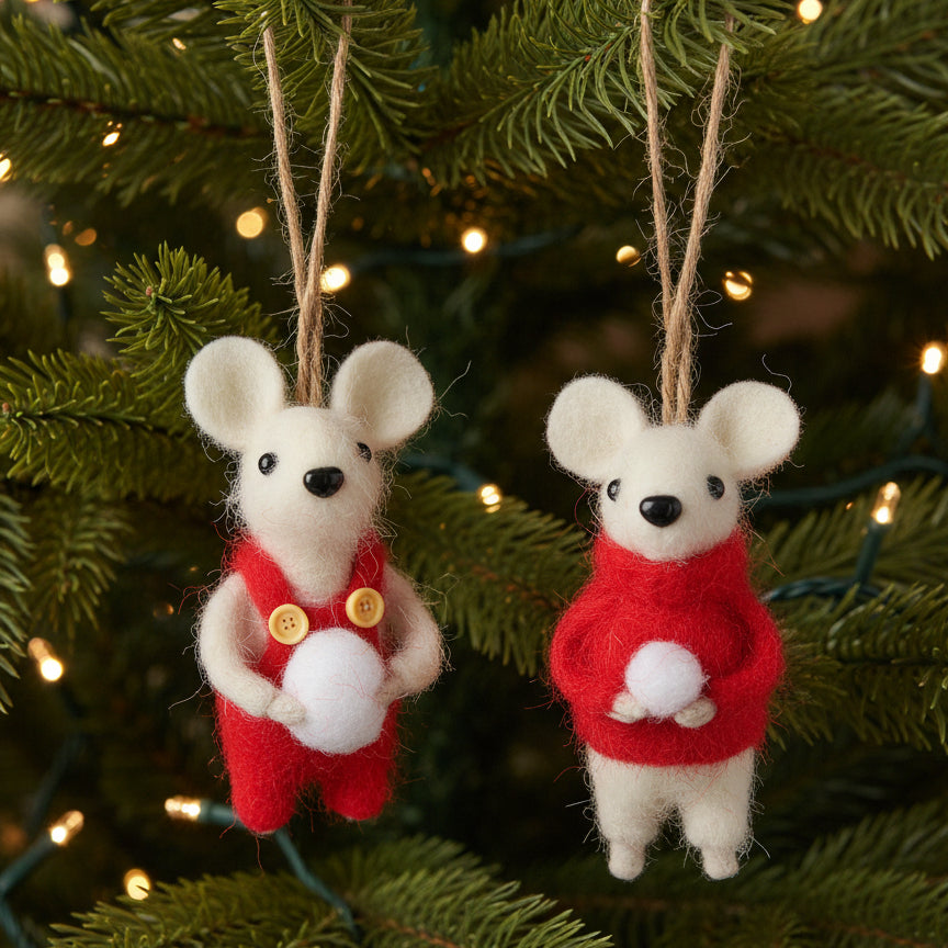 Two felted wool mouse ornaments hanging from jute strings, dressed in red outfits with one holding a white ball and the other wearing a red sweater, set against a XMAS TREE.