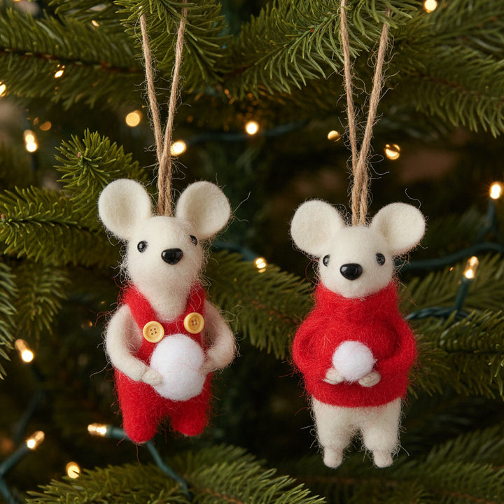 Two felted wool mouse ornaments hanging from jute strings, dressed in red outfits with one holding a white ball and the other wearing a red sweater, set against a XMAS TREE.