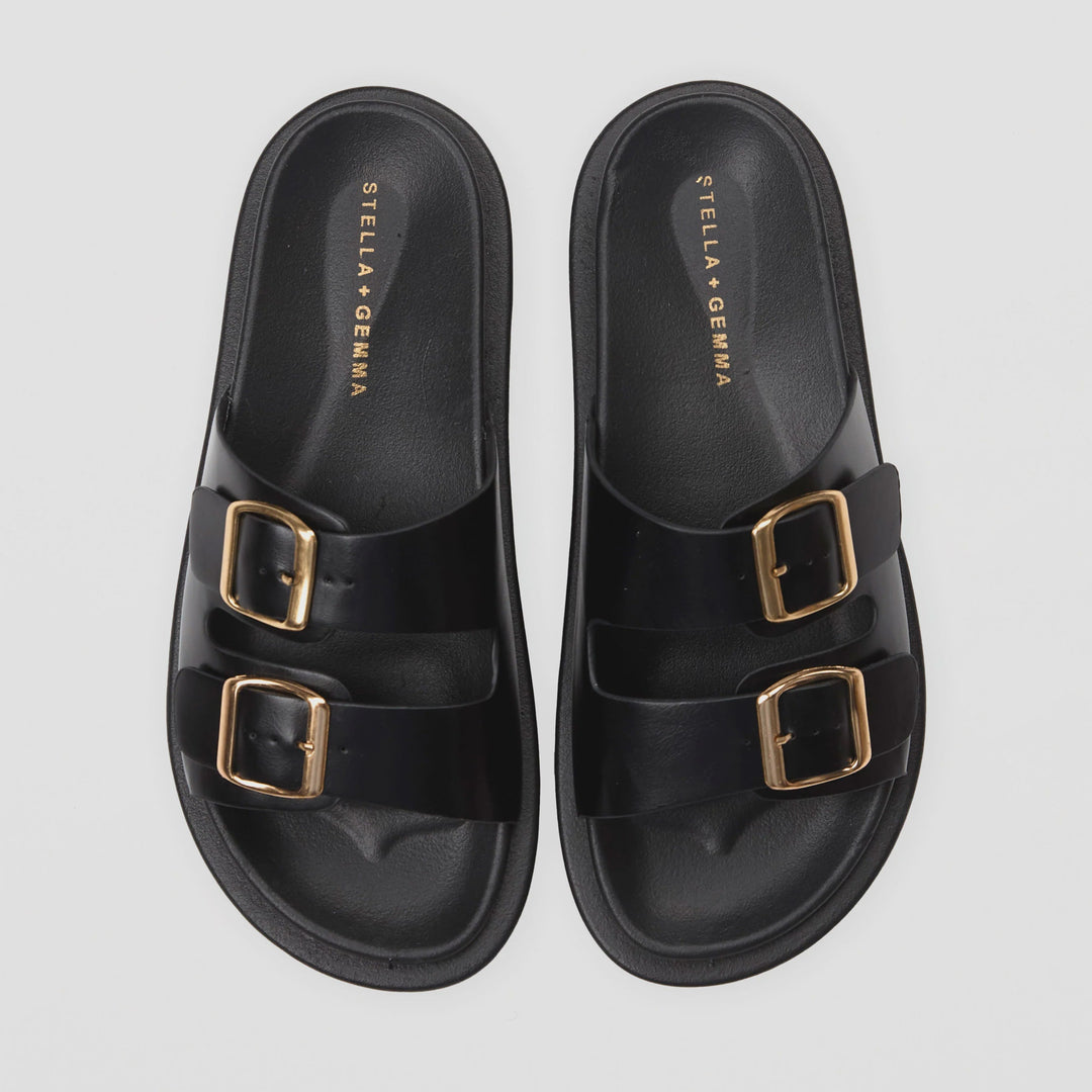 Black sandals with gold buckles on a light gray background