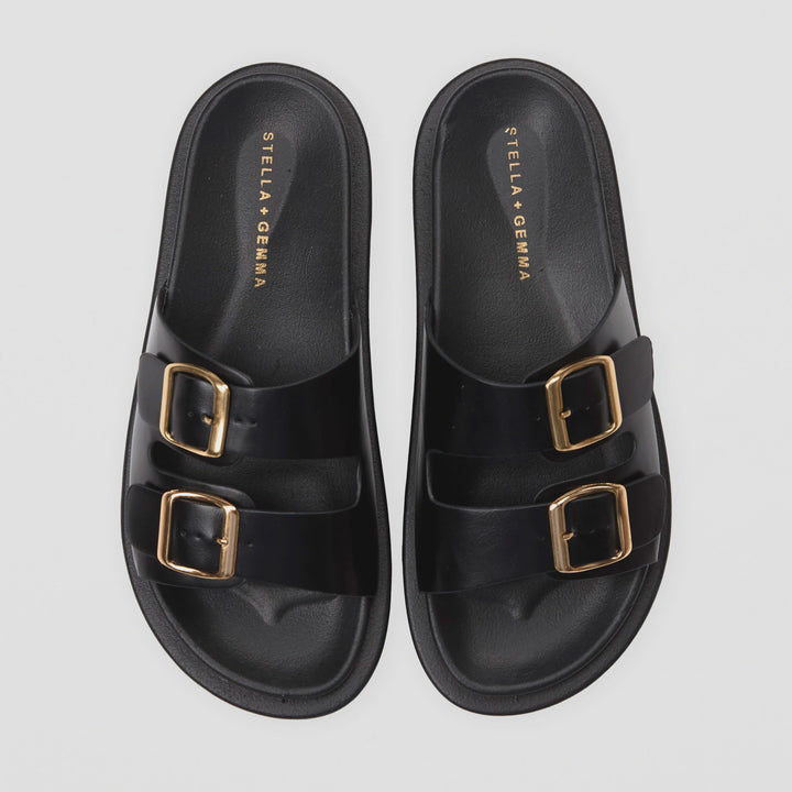 Black sandals with gold buckles on a light gray background