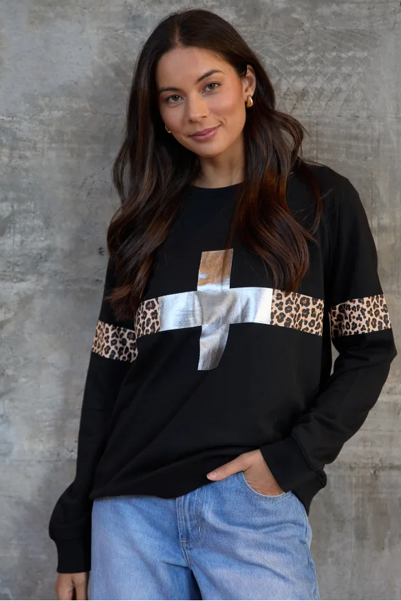 Woman wearing a black sweater with leopard print and metallic accents against a gray concrete wall.