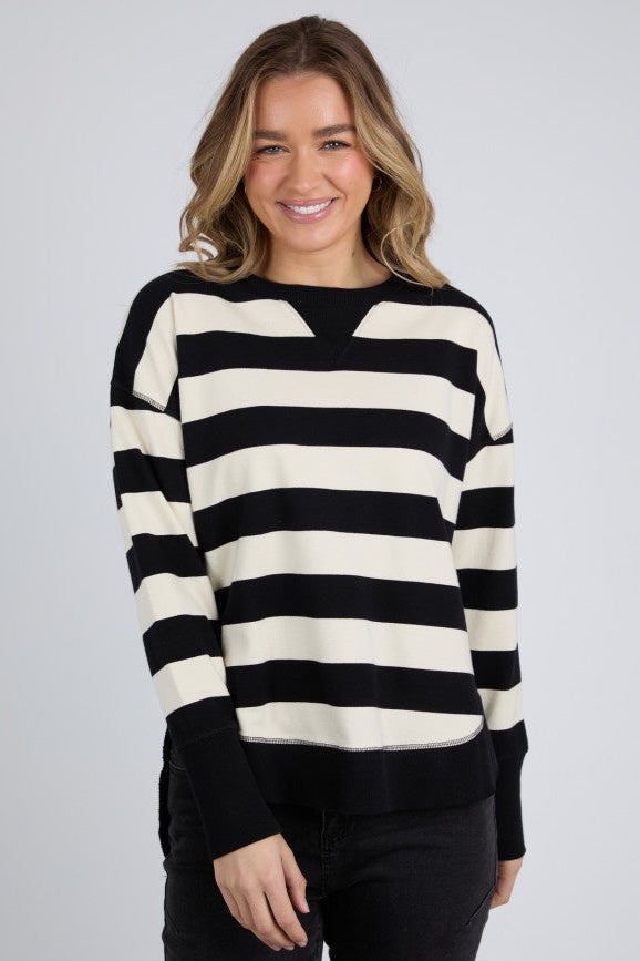 A woman smiling and wearing a black and beige striped crew neck jumper with long sleeves.