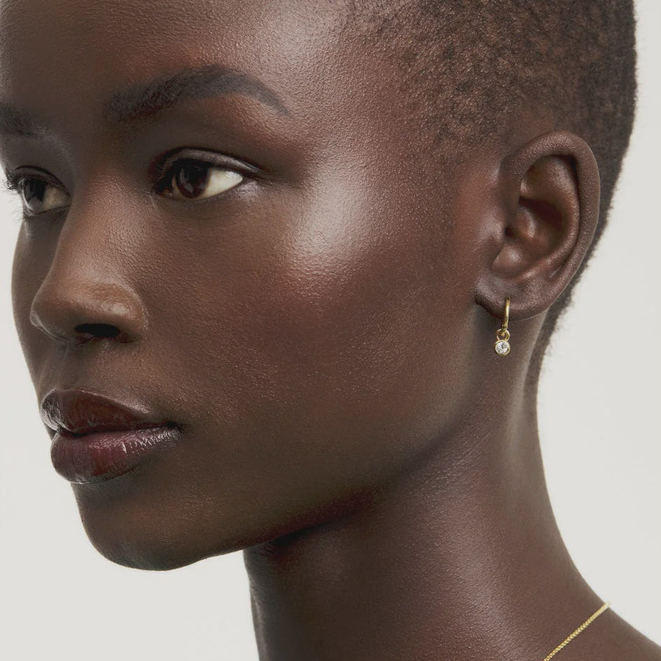 Close-up of a woman wearing a gold TED BAKER necklace and earring on a plain background