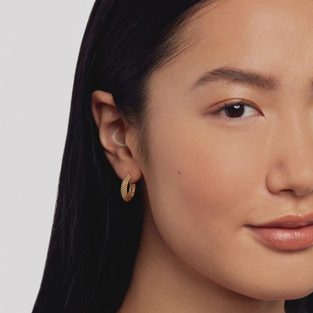 Close-up of a woman wearing gold TED BAKER hoop earrings with a plain background