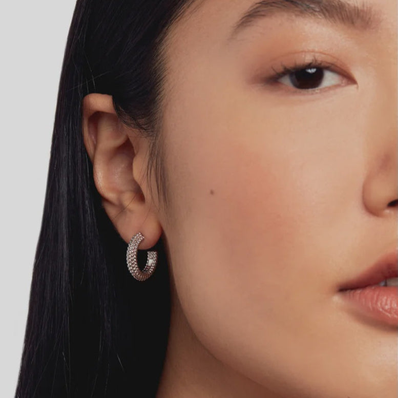 Close-up of a person wearing a TED BAKER hoop earring with a plain background