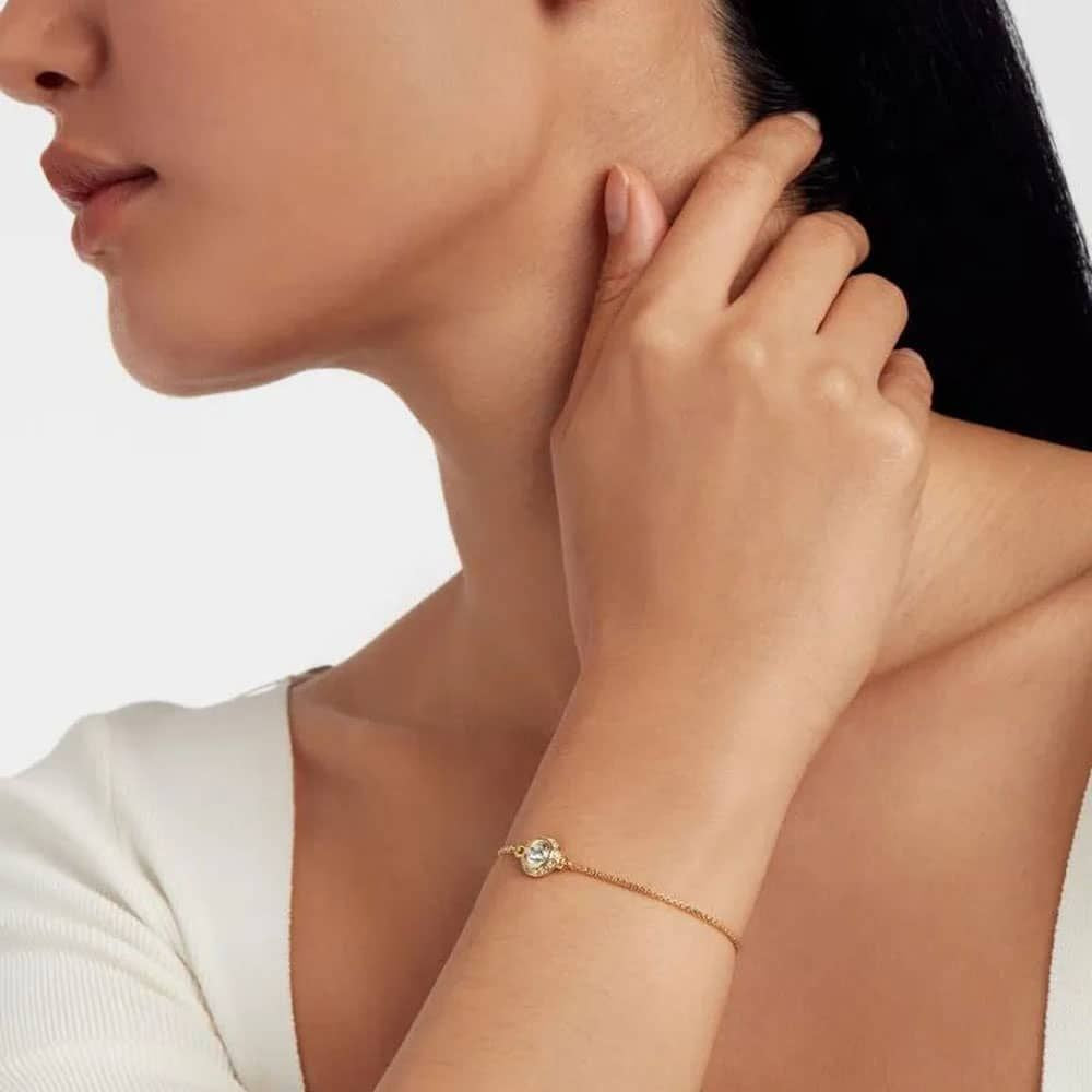 Woman wearing a TED BAKER gold bracelet on a plain background