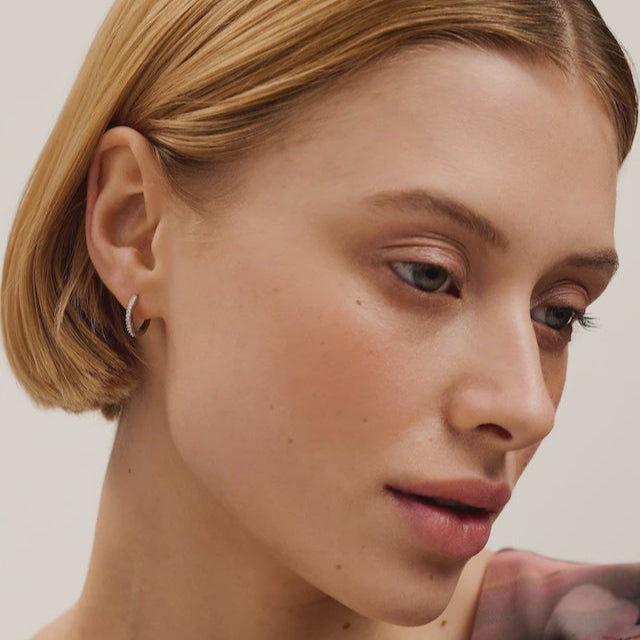Close-up of a woman with short blonde hair and a neutral expression on a plain background WEARING TED BAKER SILVER EARRINGS