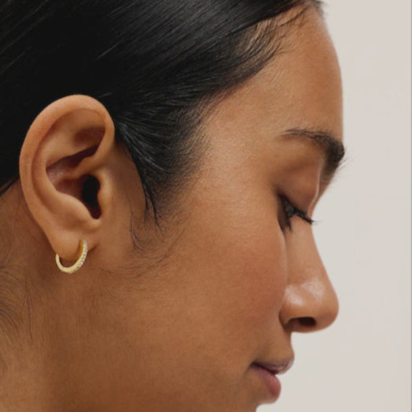 Close-up of a person wearing a gold hoop TED BAKER earring against a neutral background