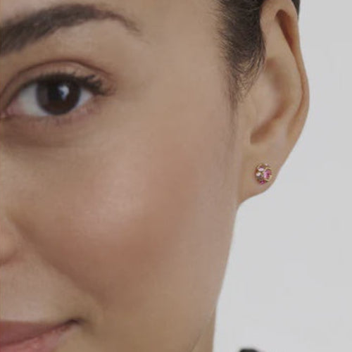 Close-up of a woman wearing a pink ted baker stud earring on a plain background