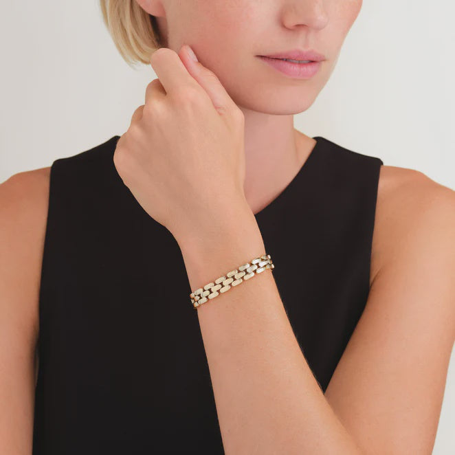 Woman wearing a gold ted baker bracelet on a plain background