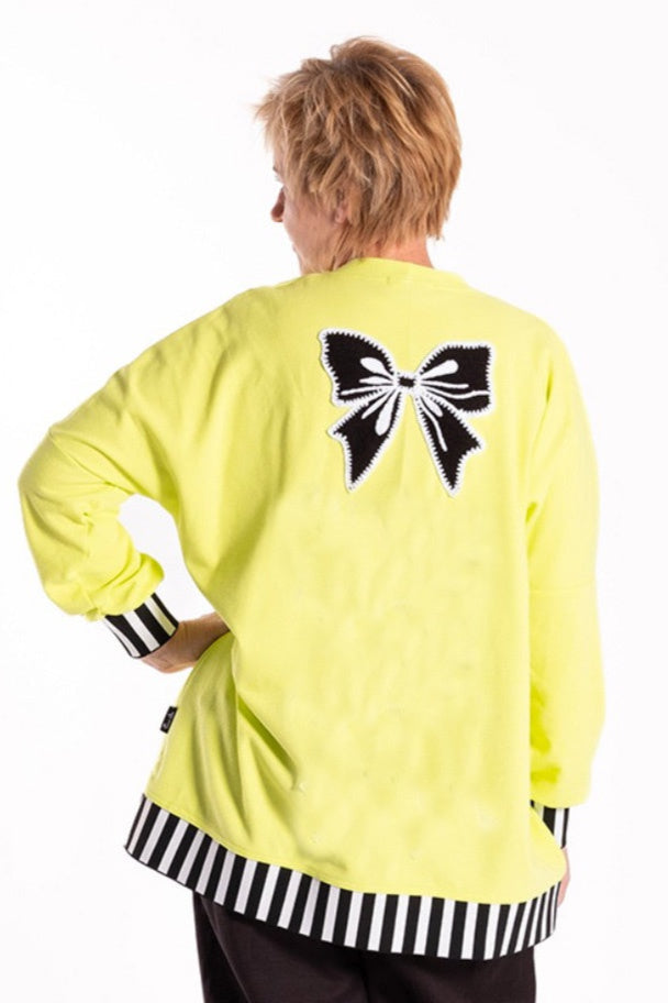 Person wearing a bright yellow cardigan with a black bow design on the back, standing against a white background.