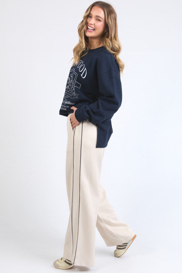 Woman wearing a navy sweater and beige pants with a white background