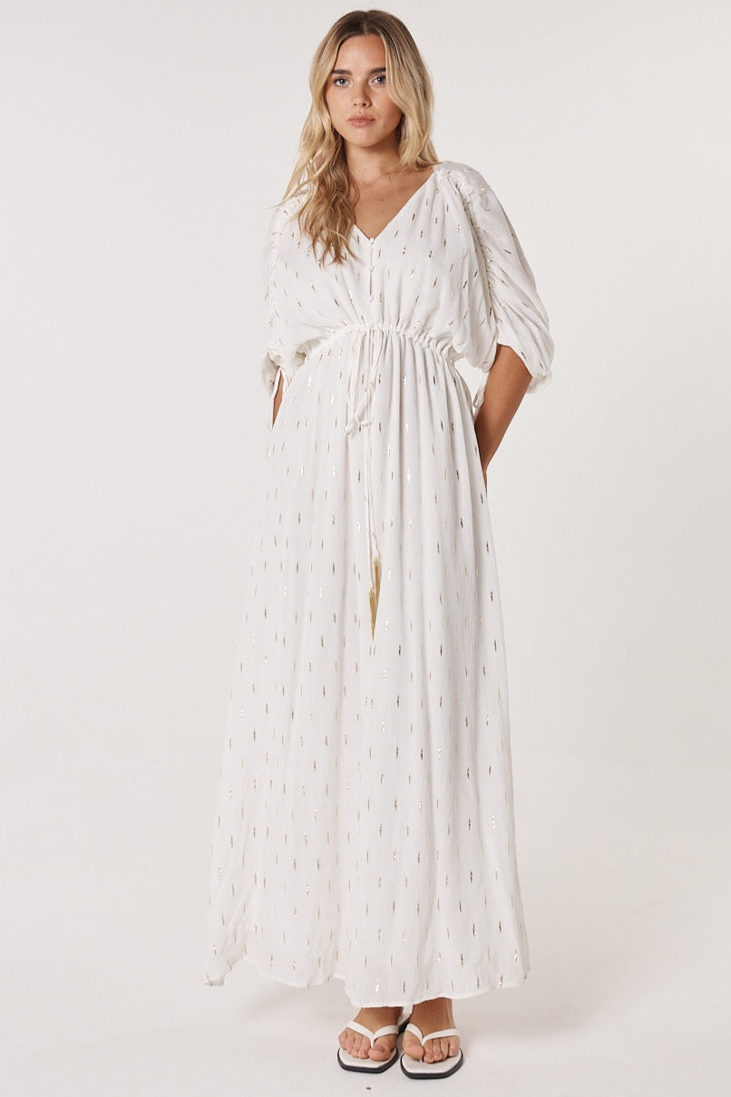 Woman wearing a fate & becker white dress with gold flecks and a waist tie with a plain background