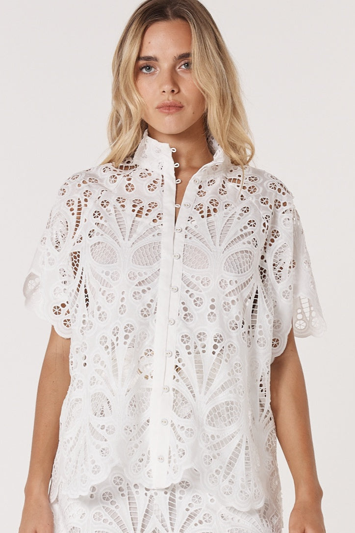Woman wearing a white lace fate & becker blouse on a plain background