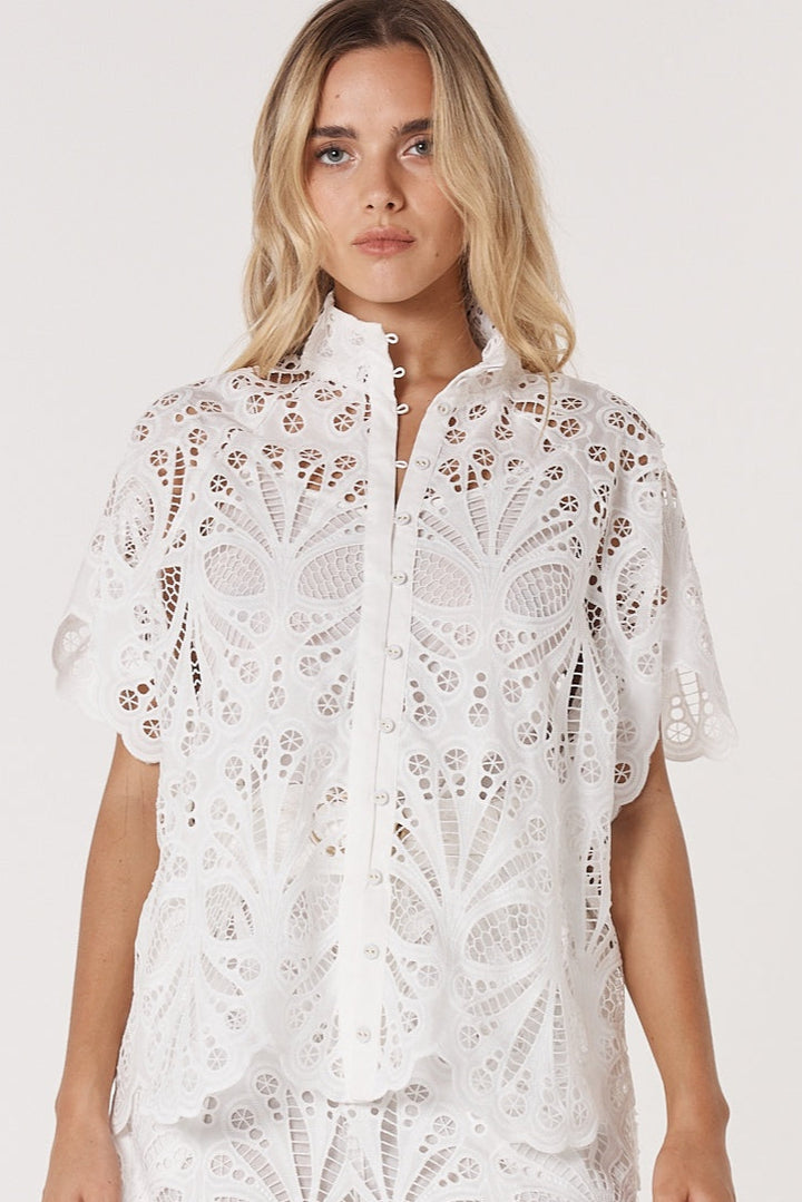 Woman wearing a white lace fate & becker blouse on a plain background