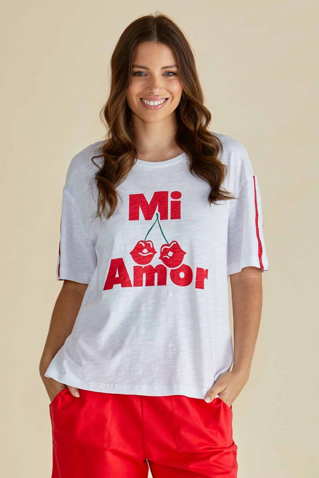 Woman wearing a white Betty Basics t-shirt with 'Mi Amor' text and red pants on a beige background