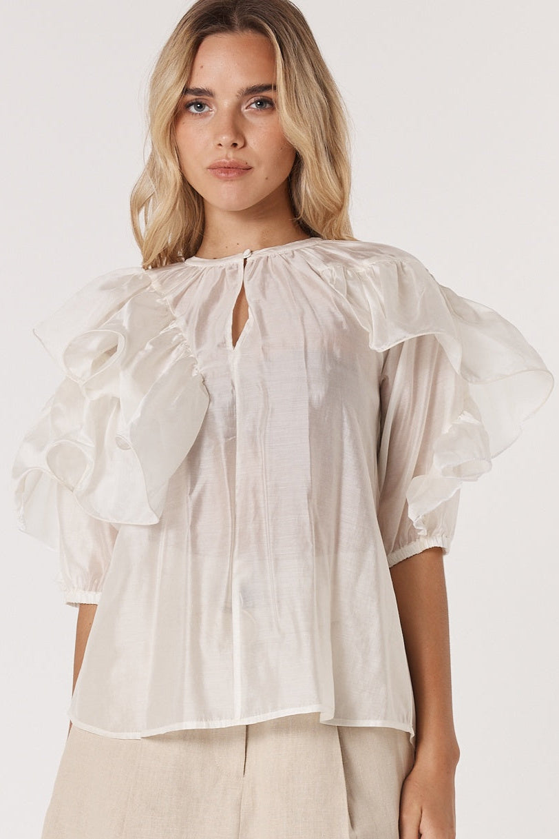 Woman wearing a light fate & becker blouse with ruffled sleeves on a white background