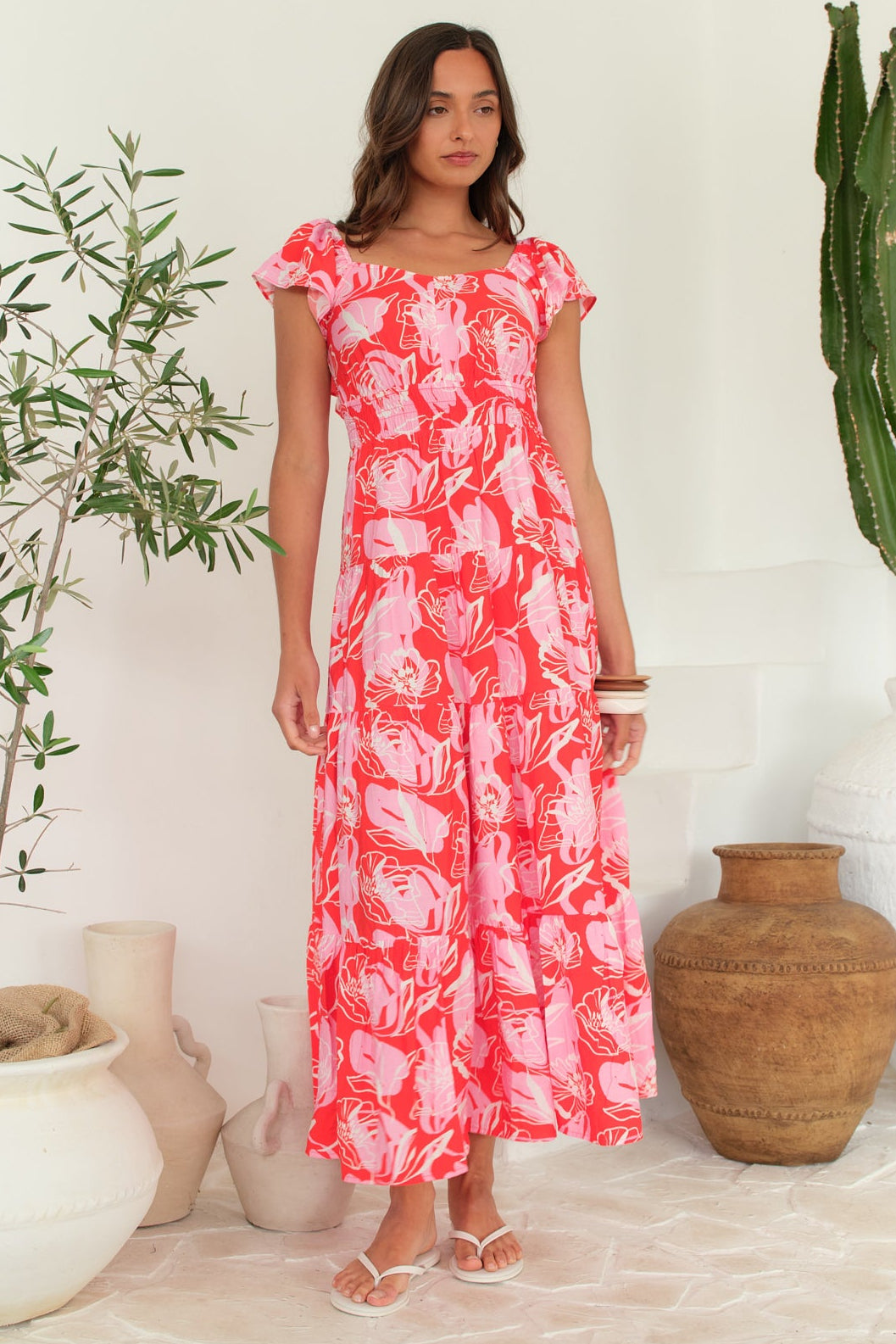 Woman wearing a pink floral dress standing in a room with plants and decorative items.