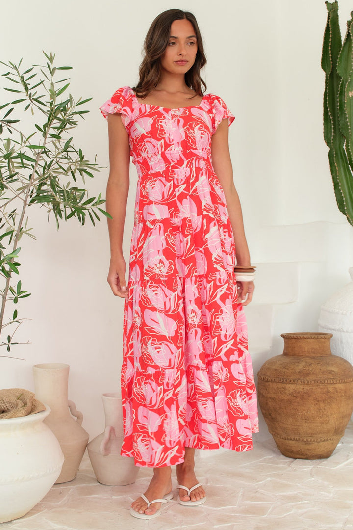 Woman wearing a pink floral dress standing in a room with plants and decorative items.