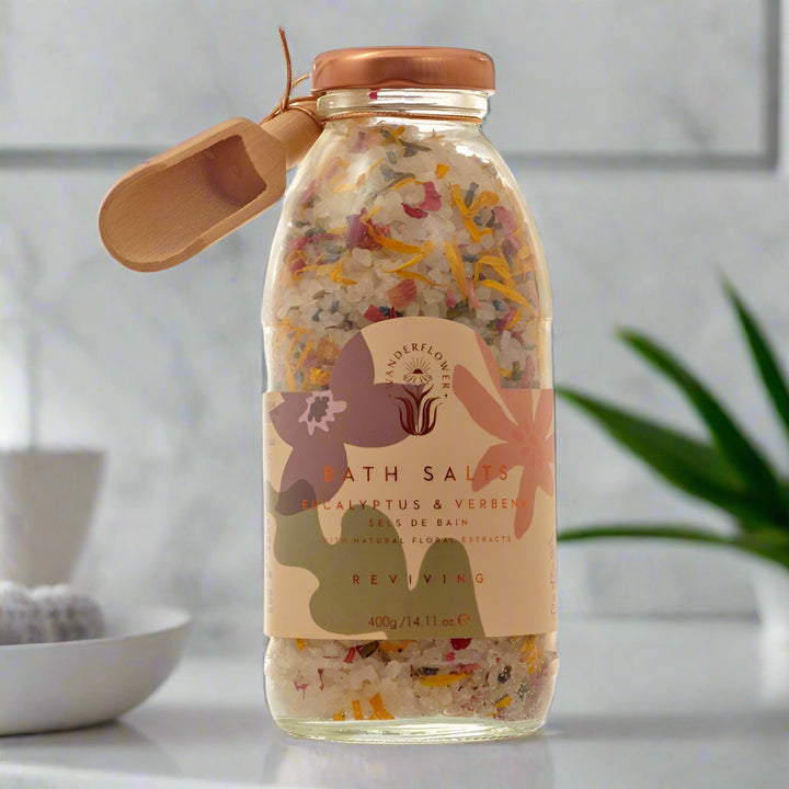 Glass jar of bath salts with a wooden scoop on a white background