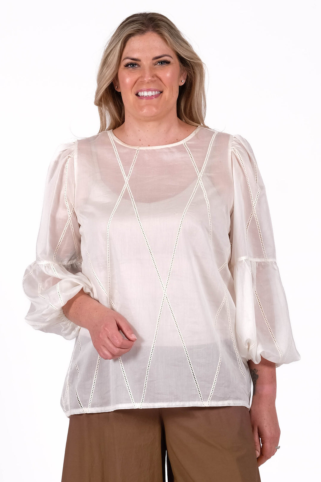 Woman wearing a white blouse and brown pants with lace details on a white background