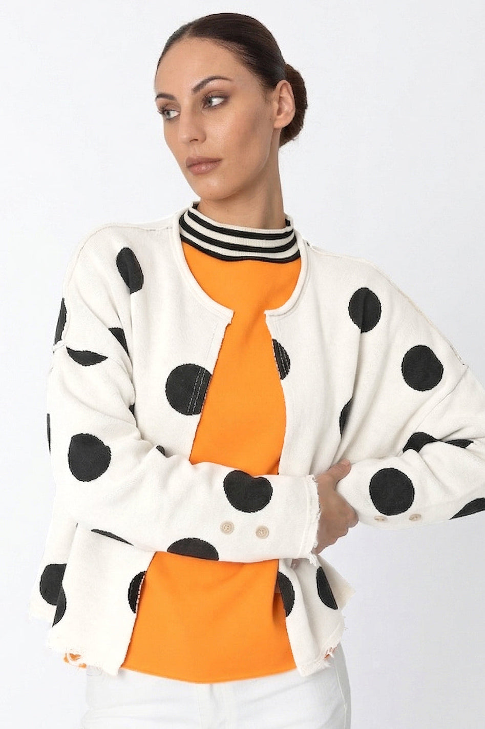 Woman wearing a polka dot cardigan over an orange top on a white background
